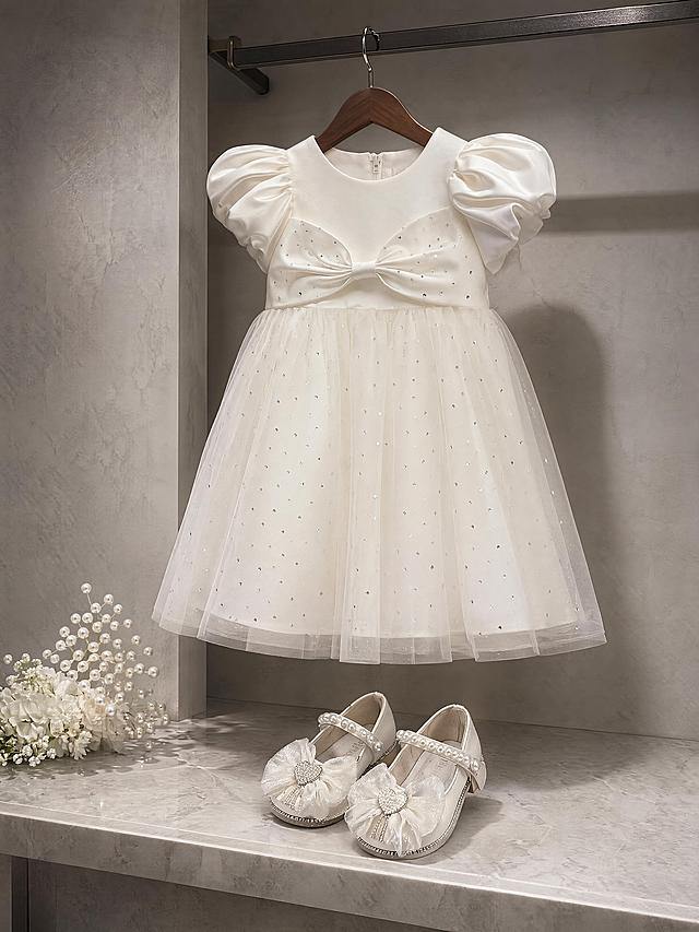 高级儿童服装展柜产品摄影。
主体：连衣裙和童鞋占画面70%，核心展示面完整不裁切，充满画面，绝对主导，近景构图。连衣裙严格参照上传产品图1，童鞋严格参照上传产品图2，完整保留所有可见组件、轮廓、结构、比例、材质、颜色、闪钻装饰与产品本体上的文字信息，与上传图完全一致；去除连衣裙上所有褶皱，保证面料平整挺括；自然融入场景光影，与场景共处同一物理空间。清除产品本体之外的多余水印和杂色信息。
呈现模式：B场景
构图与使用状态：正面平视45度视角，连衣裙悬挂在展柜挂杆，童鞋搭配陈列在连衣裙下方展示台，产品错落摆放，不发生重叠穿模。
风格：轻奢优雅
场景概念：简约欧式高级儿童服装展柜，背景保持原图风格不变，室内灯光陈列
承载与陪衬：①背景，简约欧式展柜墙面，浅灰色，哑光石膏；②底部，浅灰色大理石展示台；③点缀，一小束白色珍珠花艺装饰。
配色：主色调米白 / 浅灰 / 奶白；点缀珍珠白；画面实际颜色3种：米白 / 浅灰 / 奶白
光影：主光侧45度柔光聚光，凸显缎面网纱连衣裙流动光泽，鞋面料细腻反光，整体光影高级干净，符合展柜陈列氛围
参数：4K 写实质感，严格锁定宽高比为 3:4