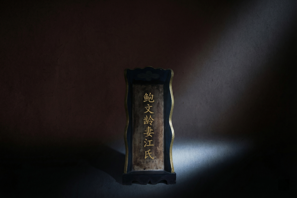 修改这张徽州清懿堂牌位照片，只保留其中一块牌位在画面中下位置，调整为特写构图，将整体背景大幅压暗变成深褐色，只留一束侧下光照亮牌位，牌位上的文字修改为“鲍文龄妻江氏”，将牌位名字改成低饱和度金色（#C预览效果