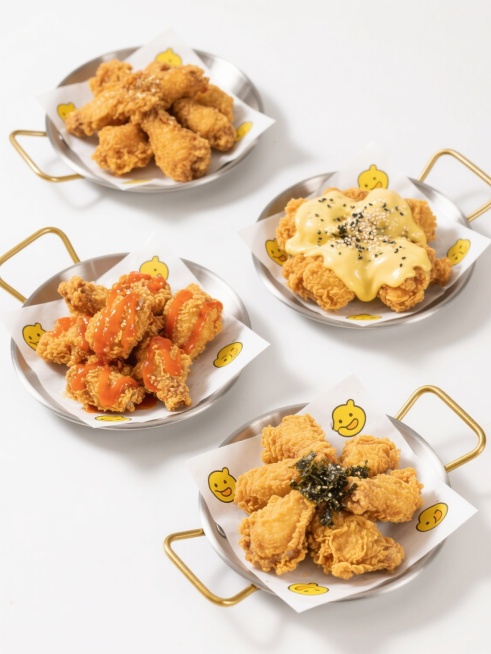 高清美食摄影，四盘不同款式、不同样式、不同配色的炸鸡，白色背景，排列整齐。炸鸡呈现出金黄酥脆的外皮质感，部分炸鸡表面淋有不同颜色的酱汁（如橙红色的韩式辣酱、奶黄色的芝士酱），撒有芝麻、海苔碎等点缀物，炸鸡块大小均匀饱满，肉质鲜嫩多汁。每盘炸鸡搭配有不同的装饰，如印有黄色卡通图案的白色油纸衬底，金属托盘带有金色把手，整体画面色彩鲜明，光影柔和，突出食物的诱人光泽和层次感，营造出美味、精致的视觉效果。预览效果