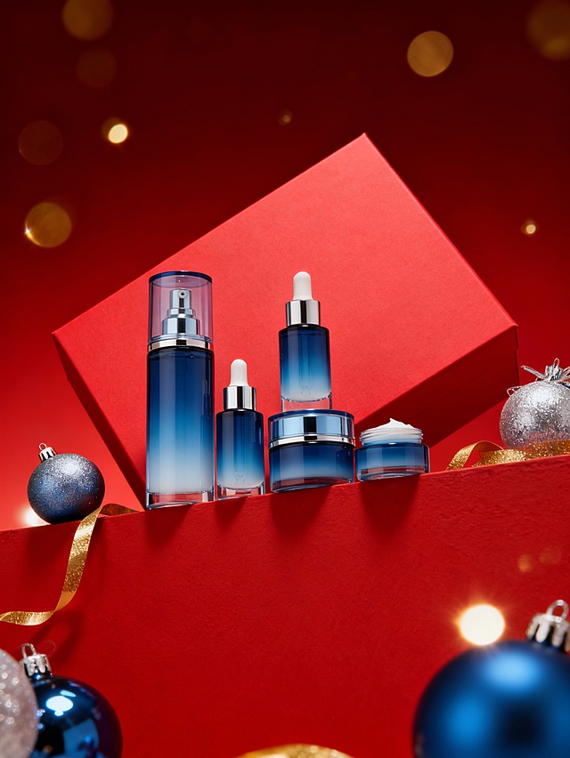 仰视角度拍摄的主体陈列在红色墙壁顶端的特写，整体偏下。背景是红色哑光礼盒呈倾斜放置在主体背后，突出商品质感。周围点缀银色和产品颜色的圣诞球，金色彩带装饰，飘落点点金色圆形亮片（虚化效果，闪闪发亮），背景为暗红色到红色的上下渐变。