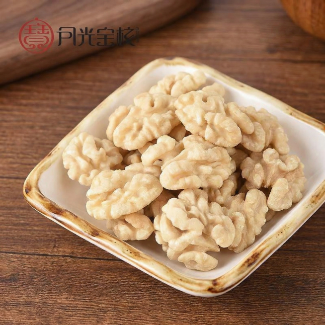 去皮核桃仁盛放做方形瓷盘里，保持产品堆叠结构、盘子样式和左上角“月光宝核”logo位置不变，替换原纯白色背景为真实干净的深棕色木质桌面背景，微距特写，柔和自然侧光，突出核桃仁新鲜饱满质感，商业美食摄影预览效果