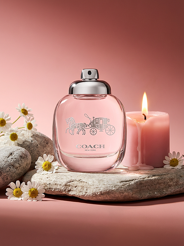 柔粉色调中，Coach香水瓶以玻璃风与浮雕工艺呈现优雅时尚，搭配雏菊与烛光，营造出甜美、温馨的实景氛围。