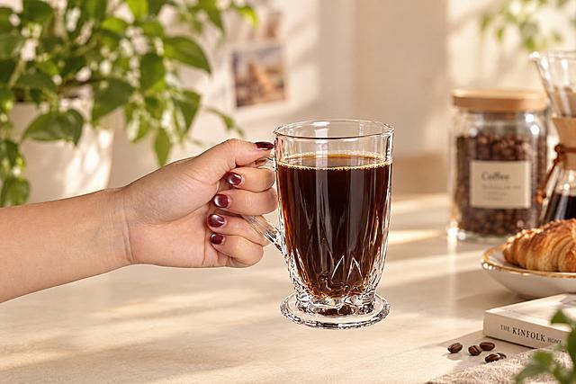 保持参考图中玻璃杯的形状、纹理、比例1:1完全不变，玻璃杯内装入深棕色美式咖啡，液面自然，咖啡质感真实通透，玻璃杯的竖纹纹理清晰锐利。保留手持玻璃杯的手部姿态和酒红色美甲细节不变。背景替换为ins风格的温馨咖啡场景，浅米色桌面，柔和自然光，背景虚化有绿植和咖啡相关小物件点缀，整体色调温暖干净，ins风高级感，4K超清画质，玻璃质感真实，光影自然柔和，商业摄影级别的高清质感