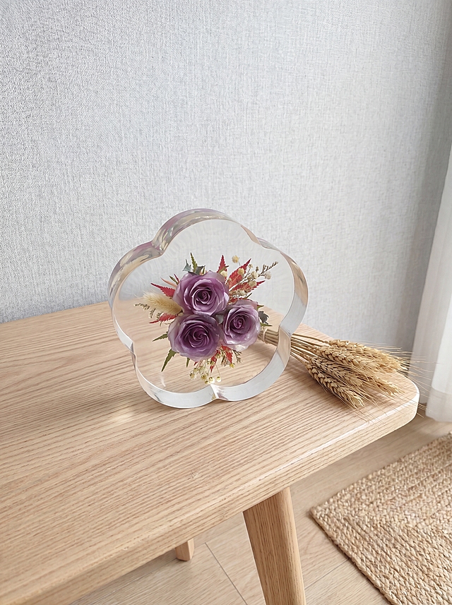 产品为梅花形树脂干花摆件，包含梅花形透明树脂块和原木底座，干花为三朵紫色玫瑰搭配狗尾草、红叶和浅色配草。保持产品主体物理结构绝对不变，不改变产品结构，产品中每张图只出现一次。树脂部分必须清亮透明犹如玻璃，画面干净无浮尘物。放置在浅原木纹理北欧风边桌上，背景是浅灰亚麻布艺墙面，角落放置天然亚麻地毯，北欧自然风空间。漫射柔和自然光，低饱和度色调，阴影清淡。三分法构图，微俯视拍摄。旁边搭配一小束天然干麦穗，增加自然生机。商业级4K摄影，画面通透干净，符合国内电商种草风格。保持3:4画面比例。负向词：西方面孔,金发,深眼窝,雀斑,杂乱房间,死黑阴影,硬光,乡村风,高对比度,欧美妆容,变形,扭曲,穿模,重叠,比例失调,浮尘,脏污,树脂浑浊,多个产品