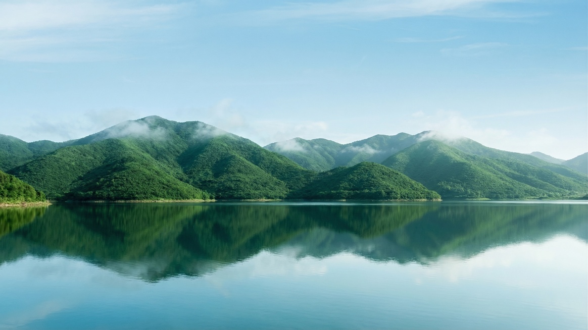 参考图片中的山水背景风格，生成类似的清新自然山水背景：淡蓝色晴朗天空，有轻薄的云雾，下方是连绵的覆盖着深绿色植被的青山，山脚下是平静澄澈的湖泊，湖面倒映着青山和天空，整体色调清新柔和，氛围静谧自然，富预览效果