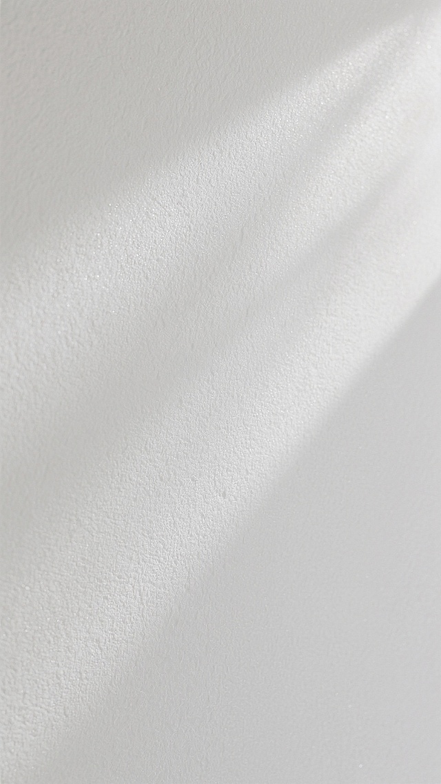 一面纯白色的墙面，表面呈现出细腻且均匀分布的磨砂质感纹理，整体视觉干净整洁，光线柔和地漫反射于墙面之上，营造出简约、素雅且略带肌理感的空间氛围，无任何图案、文字或装饰元素。