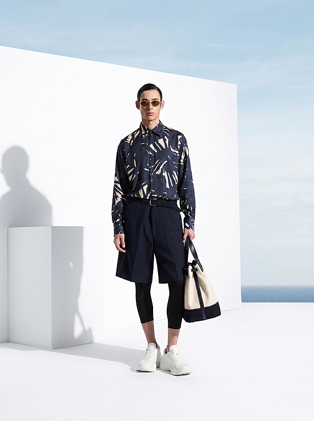 参考第一张图的场景和构图，将模特替换为第二张图的模特，保留简约白色几何背景和海景蓝天，保持高端男装广告大片风格，整体光影和构图与参考图一致