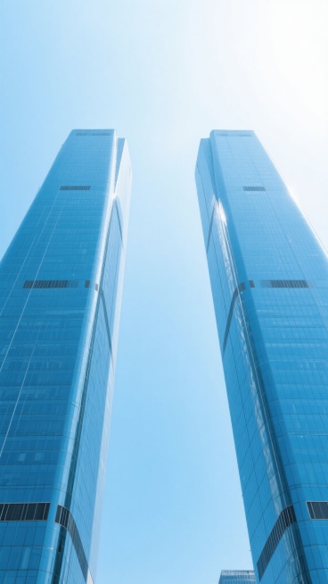从下往上仰望视角拍摄的现代城市高楼建筑群，两座高耸入云的玻璃幕墙摩天大楼占据画面主体，玻璃表面呈现出清澈的蓝色调并反射着天空的光线，大楼线条笔直挺拔，结构清晰，底部略宽向上逐渐收窄，天空背景为渐变的浅蓝色到顶部的淡白色，整体画面干净简洁，光影明亮柔和，符合现实建筑逻辑，适合作为背景素材使用。预览效果