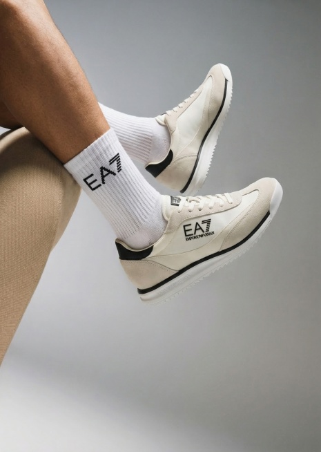参考图1的构图和样式，将图2的EA7白鞋换成模特上脚图，模特穿着这双米白色运动鞋，搭配带有EA7品牌logo的白色袜子，画面只展示从小腿到鞋子的部分，不出现完整人物，视觉聚焦在鞋子上，简约渐变灰色背景预览效果