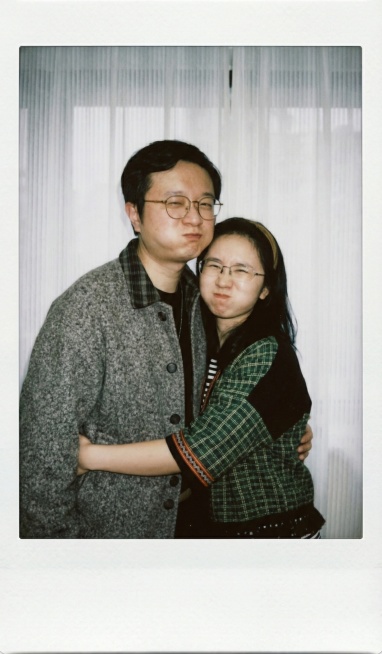 图1人物抱着图2人物，面部细节完全保留与原照片一致，使用参考图中的衣服，背景替换为质感自然的白色窗帘，呈现宝丽来相机拍摄效果，暗室闪光灯均匀柔和打光，画面清晰度一致，两人做鼓嘴眯眼的搞怪表情，拥抱姿势预览效果