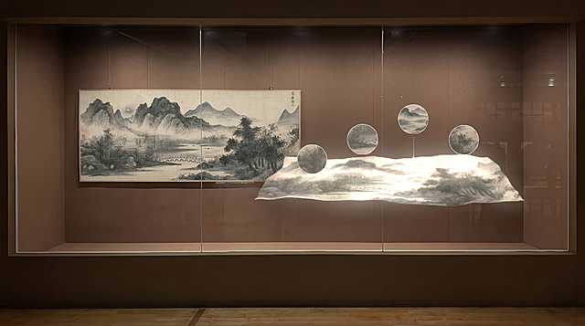 将图一展览展柜里现有的四幅古画替换为图二的水墨山水画，保留右侧玻璃上的投影，保持展柜、玻璃、展厅环境和光影不变