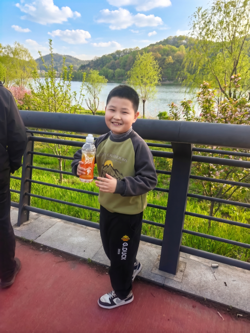 将背景美化成生机勃勃的春天景色，把枯黄的野草和树木替换为鲜嫩翠绿的绿植，整体色调清新自然，充满春日绿意，保持人物主体不变预览效果