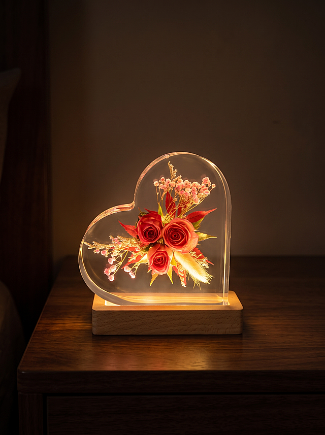 产品为心形树脂干花摆件，包含心形透明树脂块和原木底座，干花为三朵玫红色玫瑰搭配狗尾草、红叶和粉色满天星，产品自带LED发光功能。保持产品主体物理结构绝对不变，不改变产品结构，产品中每张图只出现一次。树脂部分必须清亮透明犹如玻璃，画面干净无浮尘物。放置在深色实木床头柜上，夜晚场景，四周黑暗，产品底座LED灯发出暖黄色光线，透出温暖氛围感，光线穿过透明树脂照亮干花。弱环境光，整体柔和朦胧暖调。居中平视构图。商业级4K摄影，画面通透干净，符合国内电商种草风格。保持3:4画面比例。负向词：西方面孔,金发,深眼窝,雀斑,杂乱房间,死黑阴影,硬光,乡村风,高对比度,欧美妆容,变形,扭曲,穿模,重叠,比例失调,浮尘,脏污,树脂浑浊,多个产品,明亮环境