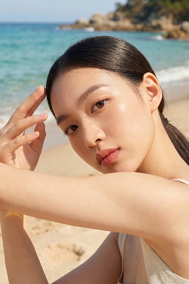 去除图片中的精华油产品，仅保留人物和手部姿势，保留海边沙滩背景，保持人物光影和整体自然风格不变，自然衔接手臂区域