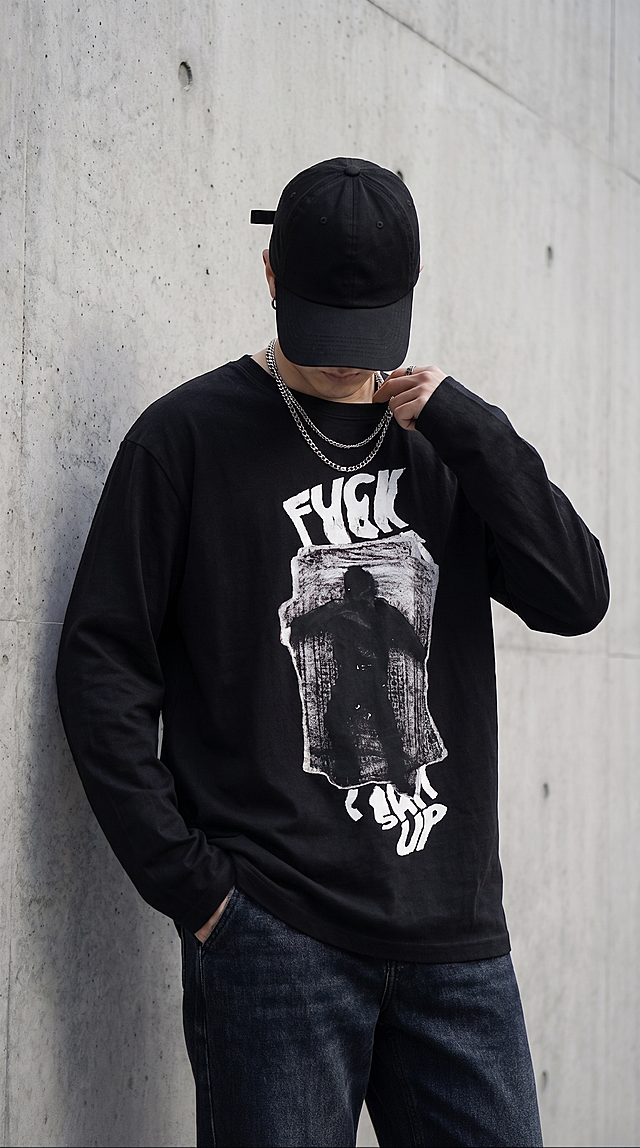 基于原图生成，更换为全新的动作和不同拍摄角度的上半身照片，保留黑色纯棉宽松长袖T恤和潮牌涂鸦印花，黑色帽子依旧压低完全遮挡脸部，搭配银饰项链，保持水泥墙面简约街头室外场景，自然光影，高级生活化色调，高清商业拍摄，突出面料质感与印花细节，中性潮酷风格，画面干净高级