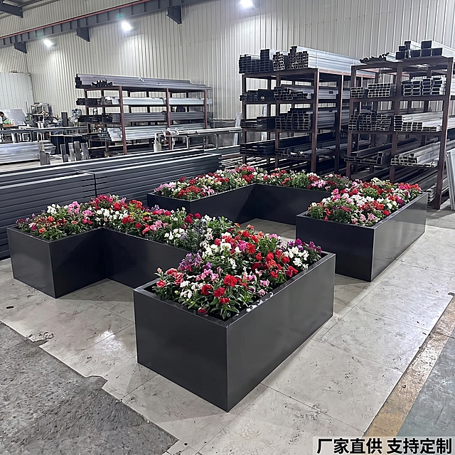 [主图-6] 黑色花箱工厂实拍图
[氛围风格] B端源头感，工厂实景
[画质] 高清商业摄影，真实自然
[元素] 三组黑色花箱摆放在工厂车间地面，背景为整齐堆放的金属型材货架，突出产品工业化生产实力. 表面光滑有金属光泽, 种植槽内种满各色鲜花（红粉/白/紫），保持产品结构、颜色、材质与输入图完全一致。
[光影] 工厂顶灯均匀照明，产品表面反光清晰，阴影柔和
[配色] 主色调黑色花箱, 辅色工业灰货架/水泥地, 点缀多彩鲜花. 颜色：黑色/浅灰/红/粉/白/紫
[视角构图] 正面平视，中景构图，完整展示三组花箱与工厂环境
[文字版式] 右下角文字“厂家直供 支持定制”，清晰不遮挡主体
[比例分辨率] 1:1比例，2k分辨率, 文字清晰超高清
[负向提示词] 变形，水印, 文字错乱, 产品模糊, 背景杂乱
