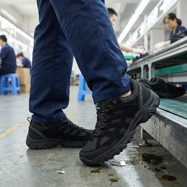 工厂流水线场景，穿着深蓝色工作服的男性工人正在工作，脚上穿着这双黑色户外徒步鞋，采用低视角拍摄，画面重点突出脚上的鞋子，鞋子细节清晰，车间光线明亮预览效果