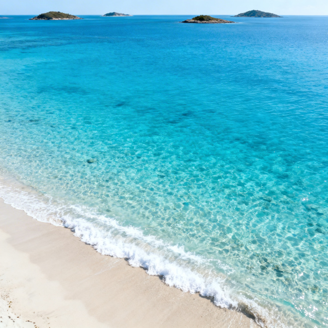 清透明亮的海湾，正上方俯视角度近景，海水清澈湛蓝，海浪轻柔拍打沙滩，远处可见零星岛屿，光线明亮通透，整体干净清新的自然风光，画质高清细腻预览效果