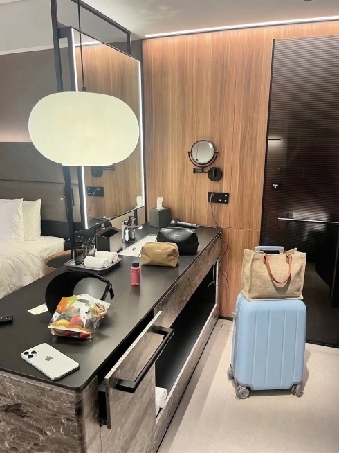 将地面的浅黄色行李箱改成浅蓝色，在浅蓝色行李箱顶上放置一个手提袋，在洗手台台面上放置两个化妆包，保持卫生间原有现代简约布局、黑木配色和光线真实自然，修改后物品与场景自然融合预览效果