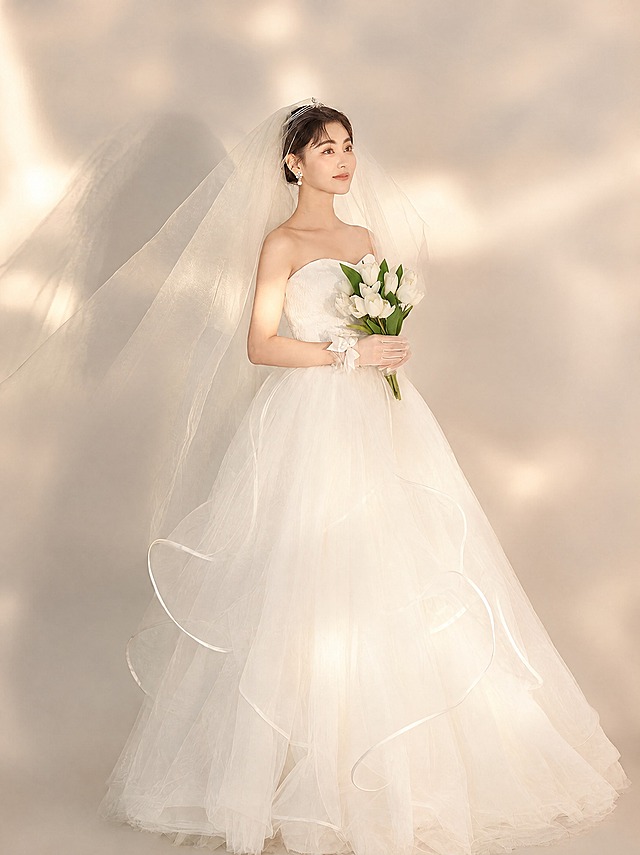 参考图中新娘的造型、婚纱款式、头纱、手持白色郁金香花束、光影效果、暖米色纯色背景整体风格不变，重新生成画面，去除图片上所有文字（包括'光影·主纱'、'Light and shadow main yarn'、'光影×极简×高级'等所有文字），保持画面干净无文字，光影柔和高级，婚纱质感细腻，人物姿态优雅自然
